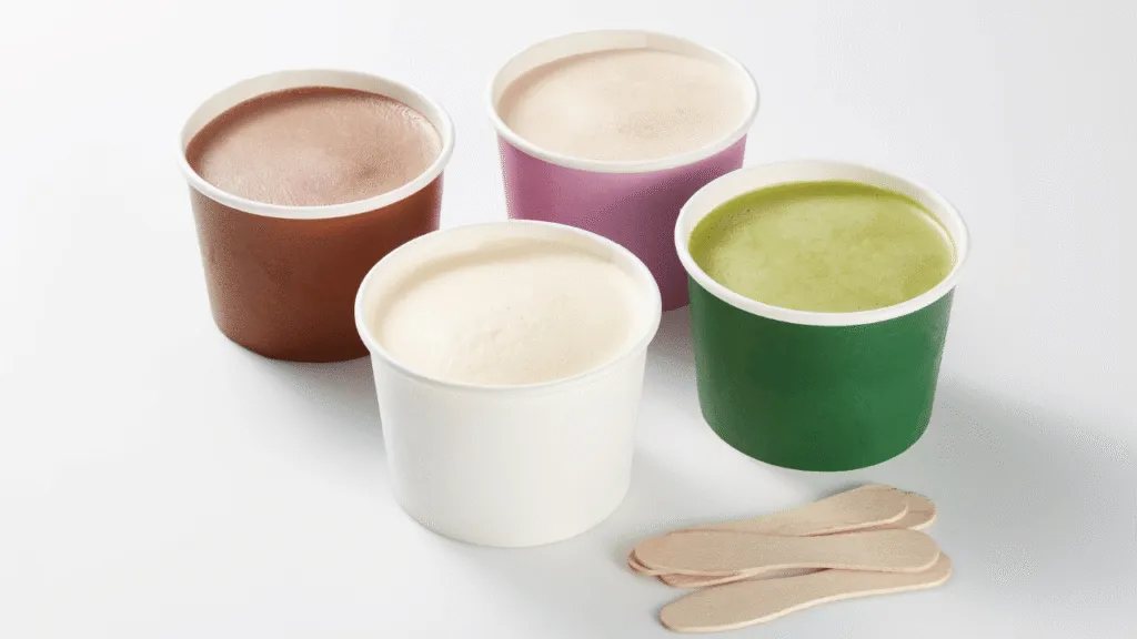 Vibrant and playful scene of Breyers ice cream pints in a cheerful kitchen setting. In the foreground, a collection of Breyers pints in various flavors are artfully arranged on a rustic wooden table, surrounded by fresh seasonal fruits, sprigs of mint, and a scattering of chopped nuts. In the middle ground, a cook's hands are mixing together a luscious ice cream-based dessert, perhaps a milkshake or sundae, using the Breyers pints as the star ingredients. The background depicts a bright, airy kitchen filled with natural light, with colorful cookbooks, utensils, and appliances hinting at the creative potential of the space. The overall mood is one of warmth, creativity, and the joyful celebration of homemade Breyers recipes. Creative Ways to Enjoy Your Pint of Breyers Ice Cream