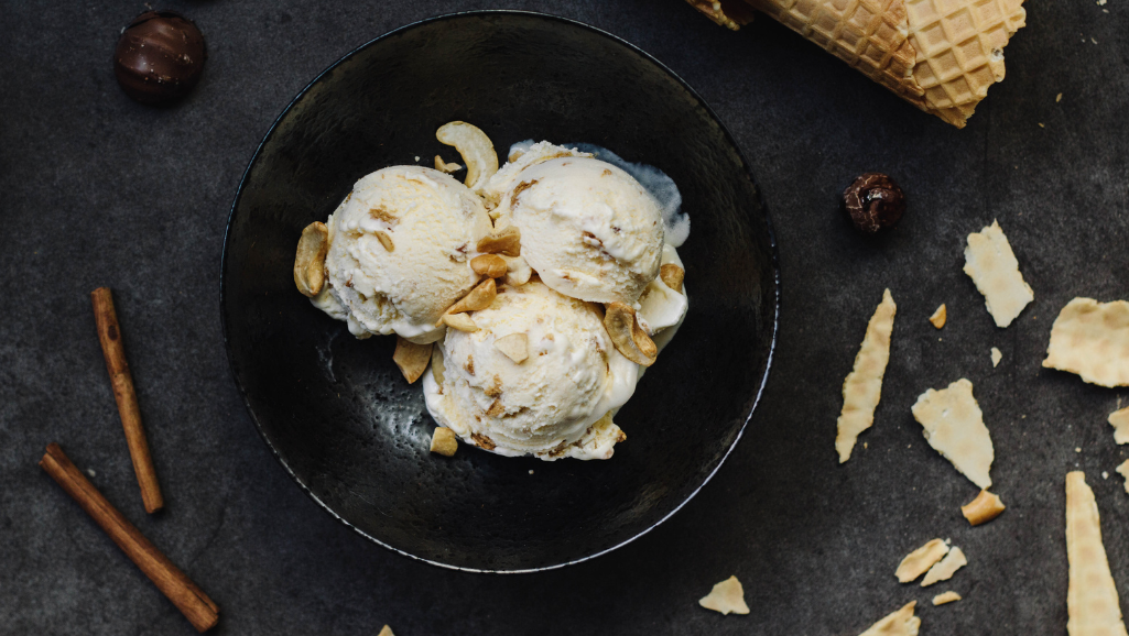 A well-lit, high-angle close-up shot of an array of essential vegan ice cream ingredients, including a bowl of creamy cashew-based base, fresh seasonal berries, a splash of vanilla extract, a sprinkling of coconut sugar, and a scattering of almond slivers. The ingredients are arranged on a clean, minimalist white surface, bathed in warm, diffused lighting that highlights their vibrant colors and natural textures. The overall composition emphasizes the simplicity and wholesome nature of the recipe, creating a visually appealing and appetizing representation of the "Creamy Eggless Ice Cream Recipe - Simple & Delicious."