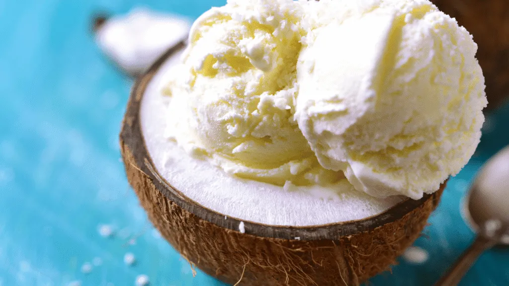 A still life capturing the essential ingredients for homemade coconut ice cream, shot on a bright, airy kitchen counter. In the foreground, a glass bowl brimming with fresh, shredded coconut and a measuring cup of rich, creamy coconut milk. In the middle ground, a stainless steel saucepan and a wooden spoon, hinting at the cooking process. The background features a glass jar of pure vanilla extract and a bag of sugar, complementing the coconut-based components. The lighting is soft and natural, highlighting the vibrant colors and textures of the ingredients. The overall composition is balanced and inviting, reflecting the simplicity and deliciousness of the homemade coconut ice cream recipe. Ingredients You’ll Need for Coconut Ice Cream Recipe