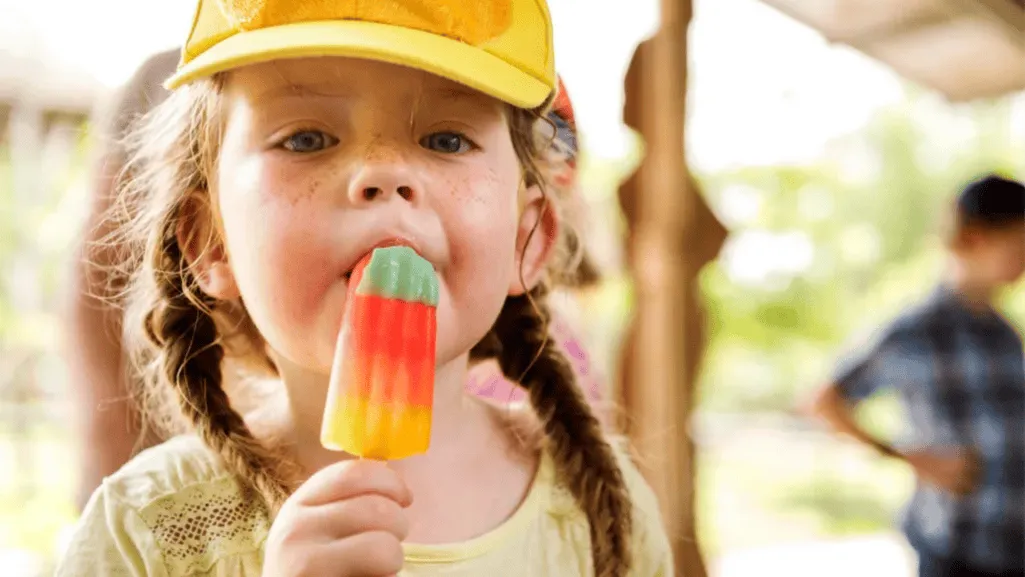 A close-up view of spoiled ice cream in a glass bowl, illuminated by warm, soft lighting. The surface appears slimy and discolored, with patches of discoloration and separation. In the middle ground, clusters of white and green mold spores dot the surface, while in the background, a blurred backdrop of a domestic kitchen suggests the familiar setting. The overall mood is one of unsettling decay, highlighting the visual indicators of spoilage that would warn a consumer against consuming the ice cream. Signs That Ice Cream Has Spoiled and Can Ice Cream Get Slimy