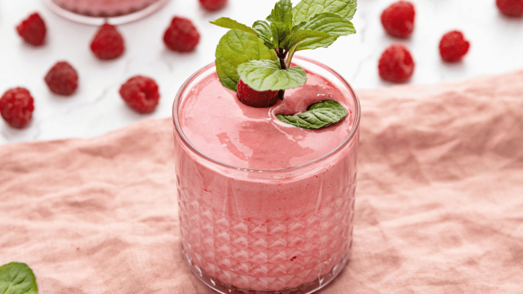 A glass jar filled with fresh, ruby-red raspberries, their plump, glistening texture inviting a taste. Beside it, a wooden spoon dips into a pool of golden honey, its viscous strands gently dripping. A sliced lemon, its bright yellow rind contrasting with the deep green stems of a sprig of mint, completes the arrangement. Soft, diffused lighting illuminates the scene, casting gentle shadows and highlighting the natural colors and textures of the ingredients. The overall mood is one of simplicity, freshness, and the inviting promise of a delicious, homemade raspberry juice. Essential Ingredients for Raspberry Juice Recipe