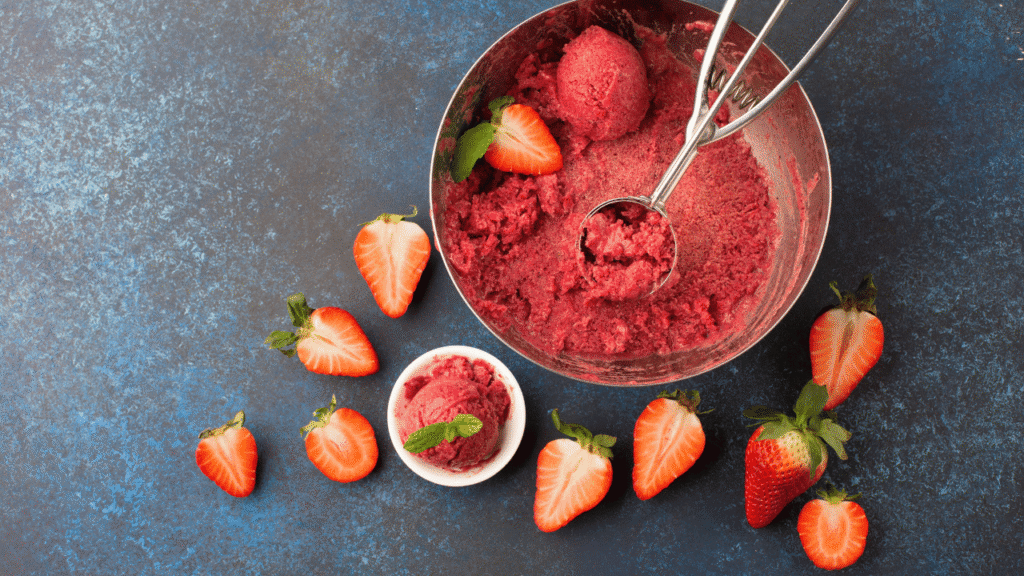 A close-up shot of a variety of fresh ingredients for homemade strawberry sherbet, arranged on a white marble countertop. In the foreground, a pile of ripe, juicy strawberries, their vibrant red hues contrasting against the clean surface. In the middle ground, a glass measuring cup filled with heavy cream, and a small bowl of granulated sugar. In the background, a stainless steel saucepan and a wooden spoon, hinting at the preparation process. The lighting is soft and diffused, creating a warm, inviting atmosphere. The overall composition emphasizes the simplicity and freshness of the ingredients, perfect for a refreshing summer dessert. Ingredients for Homemade Strawberry Sherbet Recipe