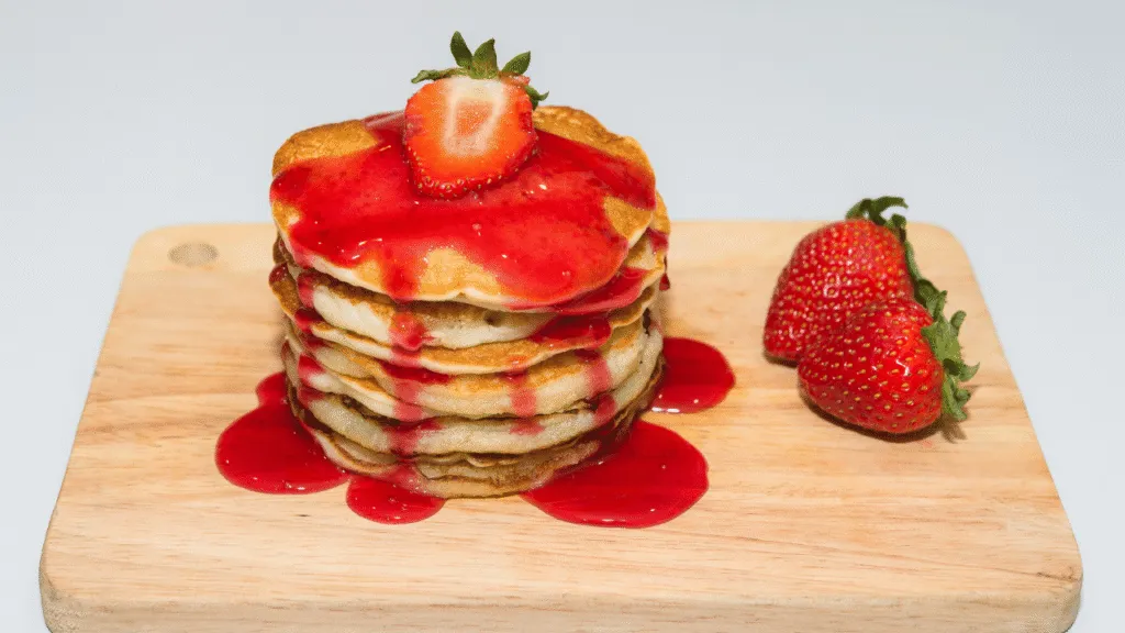 A glass container filled with thick, glossy strawberry syrup, its deep red hue glistening under warm, indirect lighting. The container sits atop a wooden surface, perhaps a pantry shelf or kitchen counter, surrounded by jars of other preserves and condiments. The overall scene evokes a sense of rustic elegance, with a focus on the vibrant color and viscous texture of the syrup, ready to be drizzled over desserts or mixed into drinks. Strawberry shortcake syrup recipe Proper Storage Techniques
