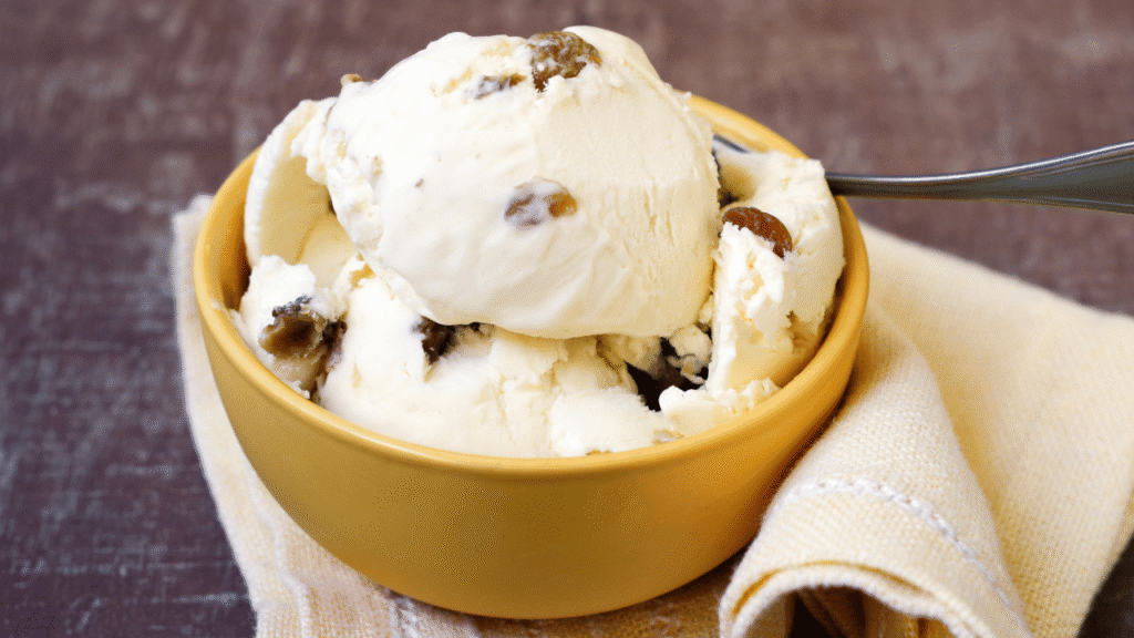 A delectable homemade ice cream, fresh from the churner, glistening with a smooth, creamy texture. Swirls of rich, golden cake batter ribbons through the ice cream, creating a decadent and nostalgic flavor. The soft scoops sit invitingly in a vintage glass bowl, bathed in warm, diffused lighting that accentuates the dessert's artisanal charm. Tiny flecks of vanilla bean and a dusting of powdered sugar add a touch of rustic elegance, while the background features a cozy, farmhouse-inspired setting, hinting at the homemade, handcrafted nature of this delightful treat. Cake Batter Ice Cream From Cold Stone Classics to Homemade Delights