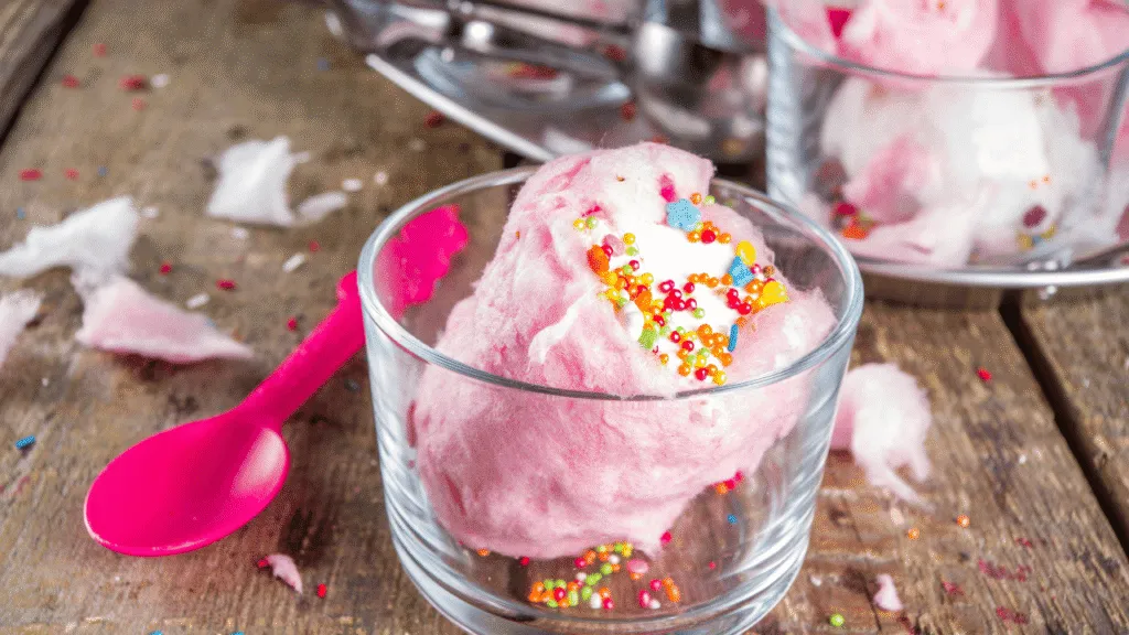A stainless steel ice cream maker sits prominently on a wooden kitchen counter, surrounded by a set of metal mixing bowls in various sizes. The machine's sleek, chrome exterior gleams under the warm, natural lighting streaming in from a nearby window. The bowls, arranged in a visually appealing manner, suggest the process of preparing the perfect cotton candy-flavored ice cream. The overall scene conveys a sense of culinary expertise and the excitement of crafting a delightful frozen treat. Cotton Candy Ice Cream Essential Equipment and Tools Overview