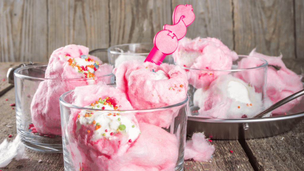 A homemade cotton candy ice cream being made in a bright, airy kitchen. In the foreground, a metal ice cream maker churns the creamy mixture, the blades catching the light and creating a swirling, cloud-like effect. In the middle ground, a chef carefully drizzles strands of vibrant pink cotton candy into the ice cream, creating a mesmerizing layered texture. The background features a clean, minimalist countertop and backsplash, allowing the focus to remain on the captivating ice cream-making process. Soft, warm lighting casts a cozy glow, and the overall scene conveys a sense of whimsical delight and homemade craftsmanship. Cotton Candy Ice Cream Recipe Step-by-Step Recipe Directions