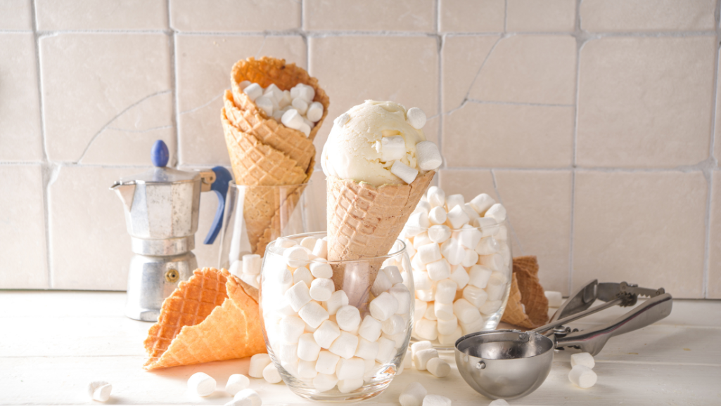 A delectable scoop of creamy marshmallow ice cream, glistening with a soft and fluffy texture, rests atop a crisp waffle cone. The luscious treat is highlighted by warm, natural lighting, casting a golden glow that accentuates its inviting appearance. In the background, a blurred backdrop of vibrant summer foliage and a clear, azure sky create a serene, idyllic atmosphere, transporting the viewer to a peaceful, sun-drenched moment. The composition is balanced, with the ice cream taking center stage, effortlessly capturing the essence of a delightful no-churn marshmallow ice cream delight.