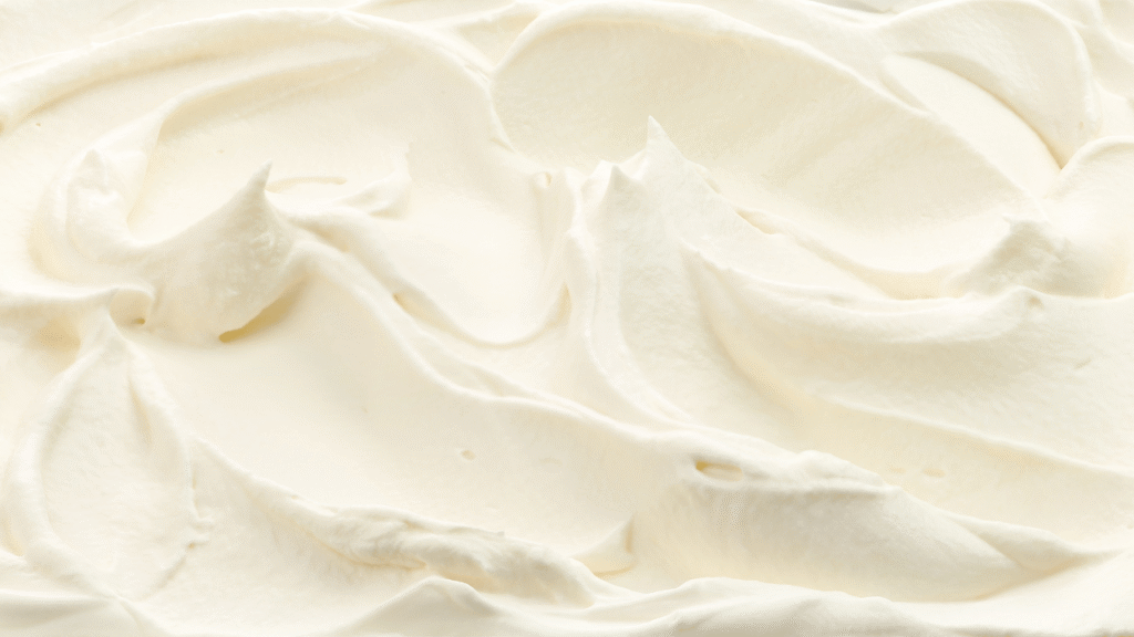 a smooth, silky ice cream base being gently blended together in a stainless steel mixing bowl, illuminated by soft, diffused natural lighting coming in from a window, creating a warm, inviting atmosphere. the creamy, off-white mixture is swirling and folding over itself, with occasional small air bubbles rising to the surface, creating a mesmerizing, hypnotic visual texture. the bowl is placed on a clean, minimalist kitchen counter, with a simple, elegant backdrop of muted tones and clean lines, allowing the focus to remain on the captivating process of crafting the perfect ice cream base. Crafting Your Perfect Ice Cream Base