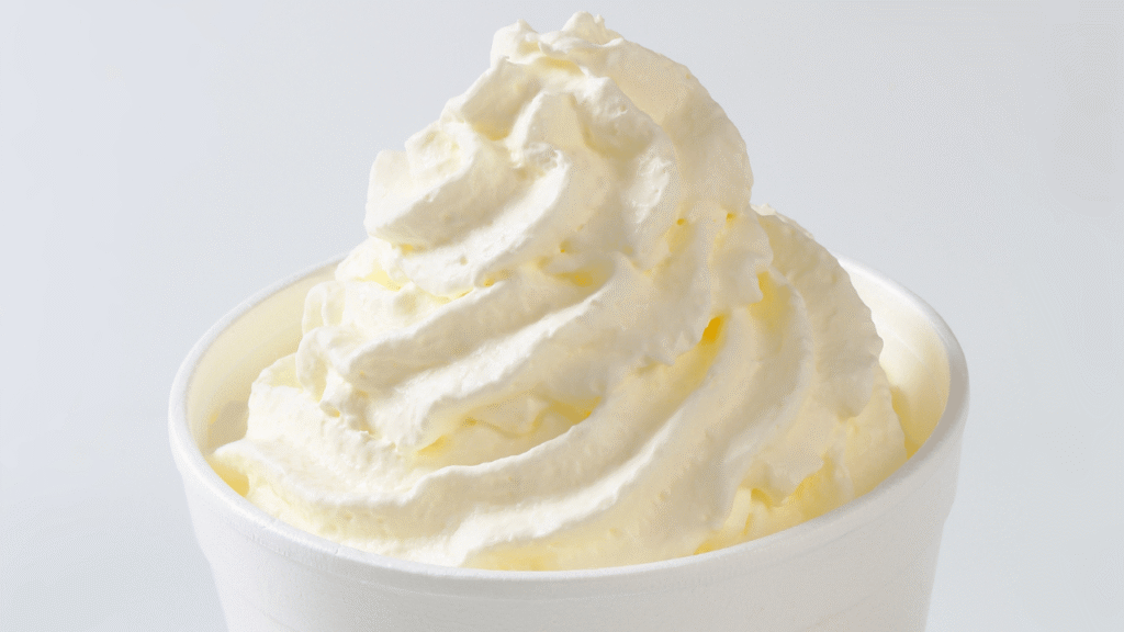 Silky, smooth, and creamy ice cream with a glossy, shimmering surface. A scoop sits in a clear glass bowl, catching the soft, warm light from above. The ice cream's texture is luxurious, with delicate ribbons and swirls that invite the viewer to dive in. The overall scene has a calming, elegant atmosphere, evoking a sense of indulgence and comfort. The camera angle is slightly elevated, creating a heightened perspective that emphasizes the ice cream's inviting, velvety appearance. Soft shadows and highlights accentuate the volume and form of the scoop, making it appear irresistibly scoopable.
