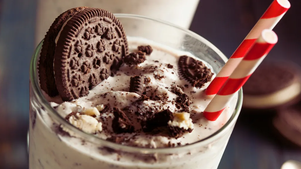 A luxuriously creamy and decadent scoop of vanilla ice cream, with swirls of rich, dark chocolate and crunchy cookie crumbs throughout. The ice cream is slightly melted, giving it a glossy, indulgent sheen under the warm, soft lighting. The scene is captured from a low angle, emphasizing the towering height of the treat and the tempting textures. The background is blurred, keeping the focus solely on the delectable dessert, evoking a sense of irresistible indulgence.