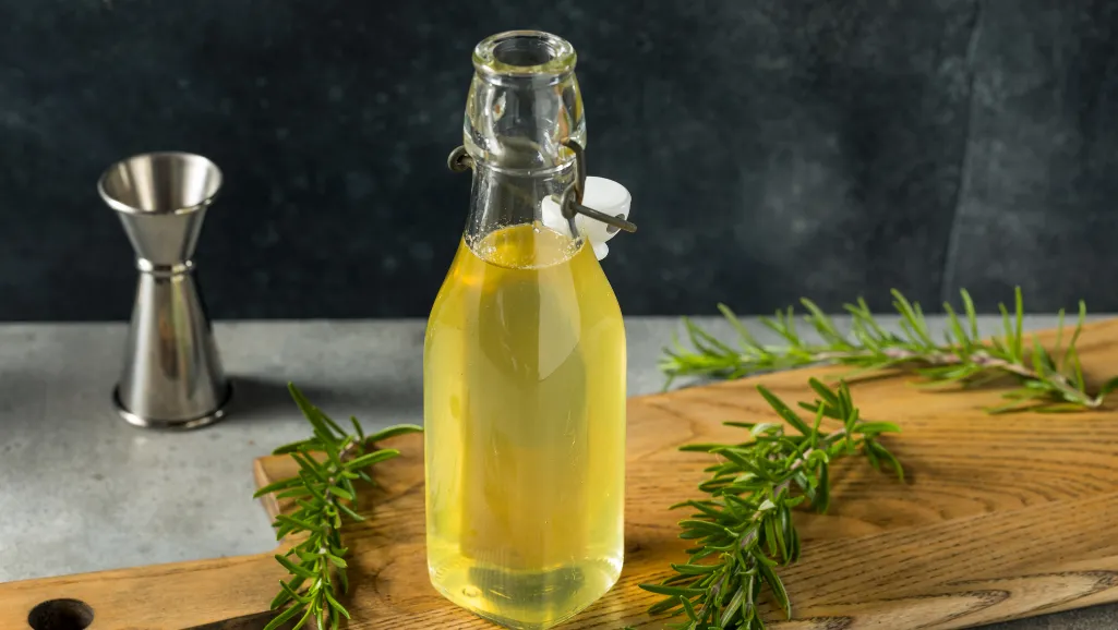 A cozy kitchen countertop bathed in warm, natural lighting. In the foreground, a sleek glass bottle filled with a vibrant green rosemary simple syrup, accompanied by fresh sprigs of rosemary. Alongside, an assortment of glassware - tumblers, highball glasses, and wine glasses - each containing a different rosemary-infused beverage, from a refreshing rosemary lemonade to a sophisticated rosemary-tinged gin and tonic. The middle ground showcases a variety of fresh citrus wedges, crushed ice, and botanical garnishes, hinting at the versatility of this aromatic syrup. In the background, a subtle backdrop of wooden shelves and minimal kitchen decor, creating a serene, inviting atmosphere.