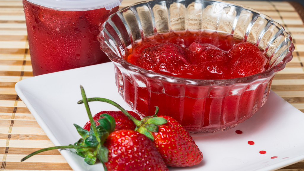 A well-lit kitchen counter, the surface glistening with a light sheen. In the foreground, a saucepan simmers, steam rising as a spoon slowly stirs the clear, viscous liquid – a homemade fruit syrup in the making. The pan is surrounded by an array of fresh, vibrant berries, their colors a visual feast. Soft, diffused lighting casts a warm glow, highlighting the textures – the smooth glaze of the syrup, the firm flesh of the berries, the polished wood of the counter. The scene conveys a sense of care and craftsmanship, inviting the viewer to experience the art of texture control in creating a delectable, pourable fruit syrup.