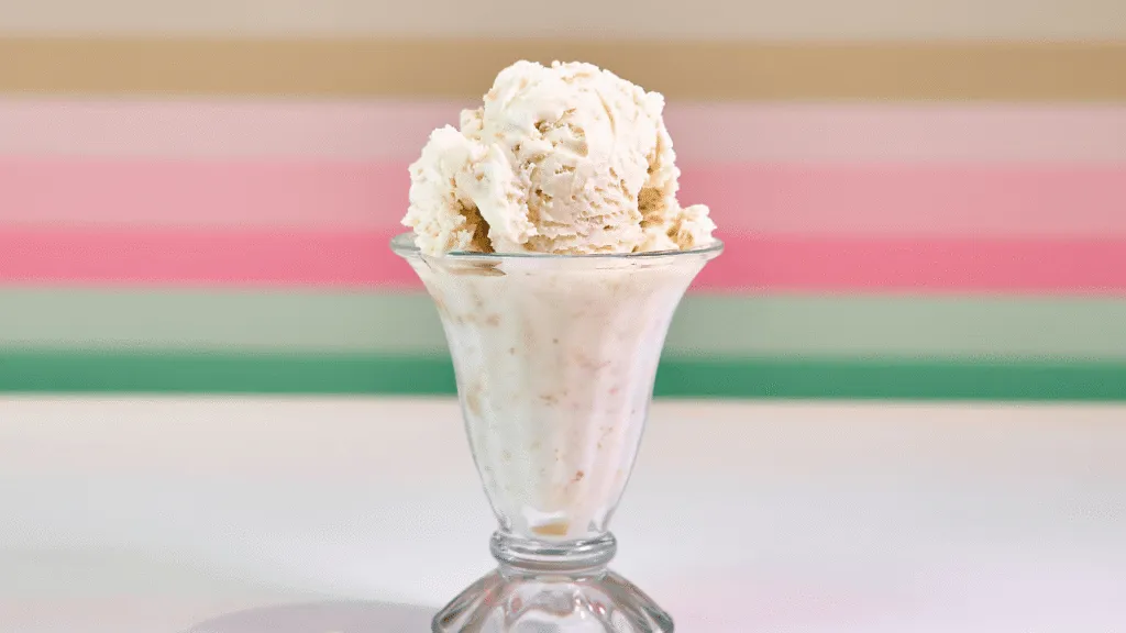 a closeup photograph of a creamy, pale yellow-colored ice cream base, smooth and velvety in texture, with a slight sheen on the surface, set against a dark background with soft, warm lighting from the side, creating a dramatic chiaroscuro effect that highlights the rich, luxurious quality of the ice cream, the composition focused on the texture and color of the base, with a sense of depth and dimension, evoking the indulgent, comforting nature of homemade Thai tea ice cream. Thai Tea Ice Cream Recipe