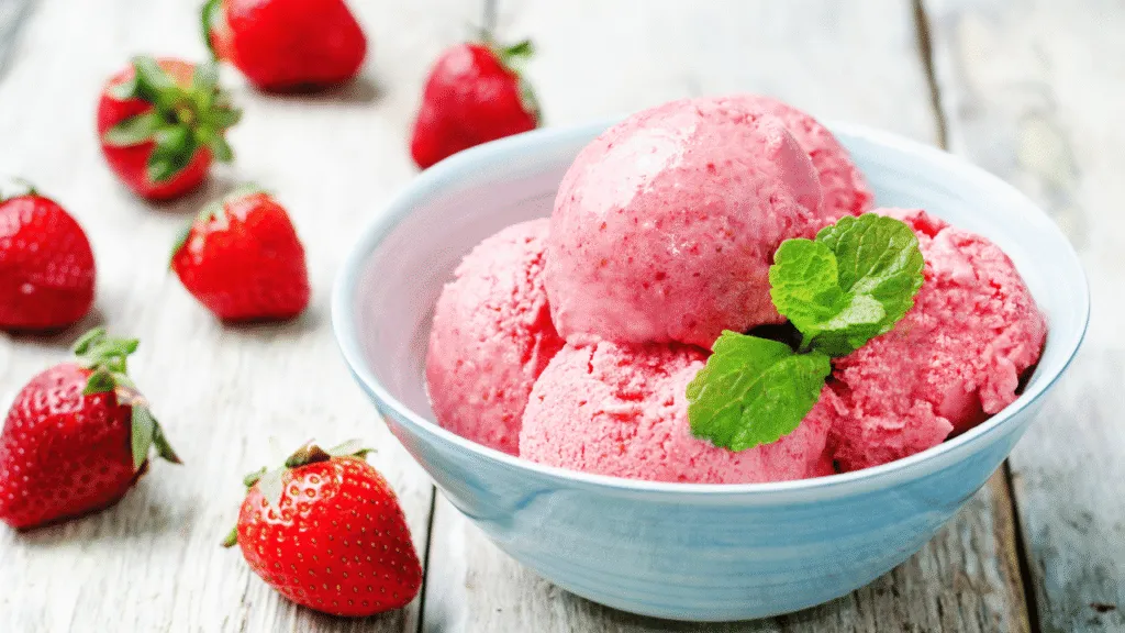 A sleek, stainless steel ice cream maker sits on a rustic wooden countertop, its chrome surfaces gleaming under soft, diffused lighting. Fresh, plump strawberries are neatly arranged around the machine, their vibrant red hues and luscious texture hinting at the homemade treat to come. The background is a clean, white space, allowing the ice cream maker and its mouthwatering ingredients to take center stage. The scene conveys a sense of simplicity, quality, and the classic pleasure of making a timeless strawberry ice cream recipe in the comfort of one's own kitchen. classic strawberry ice cream recipe: step-by-step instructions