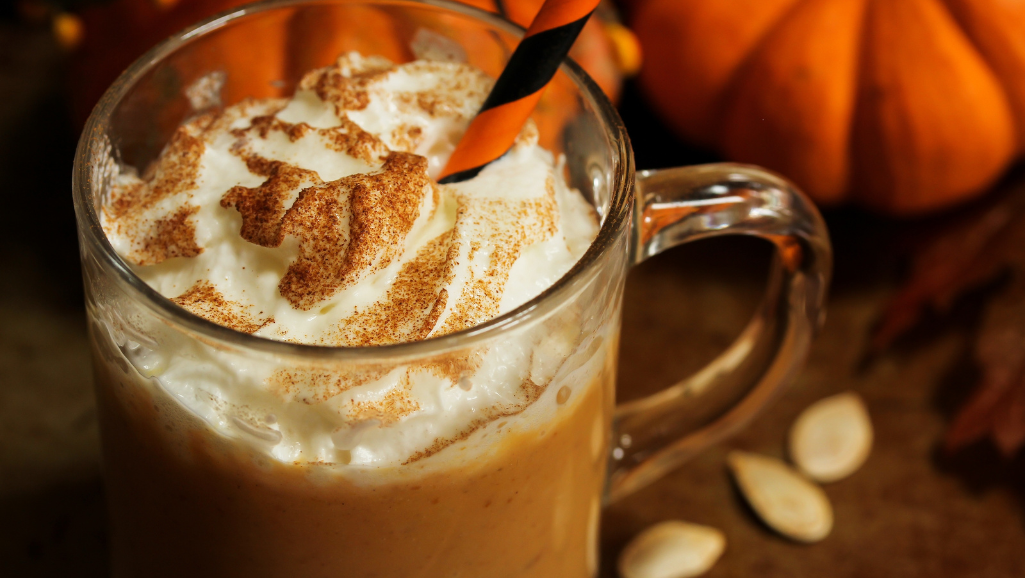 A creamy, dreamy scoop of pumpkin spice latte ice cream, its rich orange hue swirled with espresso-infused ribbons and topped with a dollop of whipped cream. The light plays across the smooth, glossy surface, casting delicate shadows that accentuate the velvety texture. Crisp autumn leaves in vibrant reds and golds form a natural backdrop, hinting at the cozy, nostalgic atmosphere of the season. Soft, diffused lighting from an unseen source casts a warm, inviting glow, making this frozen treat look utterly tempting and irresistible.