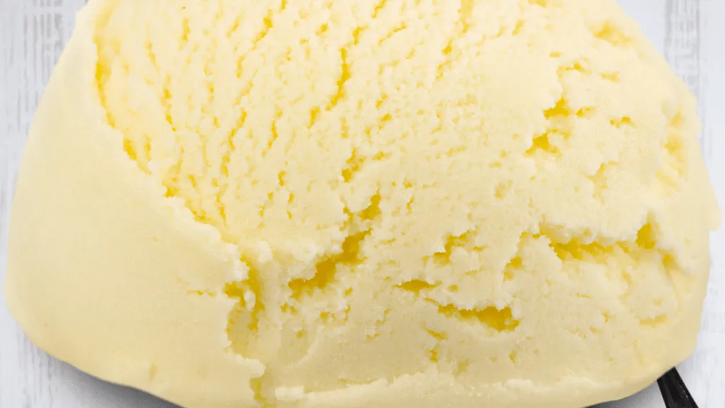 A gleaming stainless steel ice cream maker set against a backdrop of white tile countertops. The machine's sleek curves and brushed metal finish catch the warm glow of overhead track lighting. Dials and switches stand ready to control the churning action, while a clear plastic dome reveals the frozen treat taking shape within. Surrounding the appliance, a selection of elegant porcelain ramekins and tasting spoons await the first taste of the creamy, indulgent dessert. Baileys and Ice Cream Recipe Essential Tools and Ice Cream Maker Prep