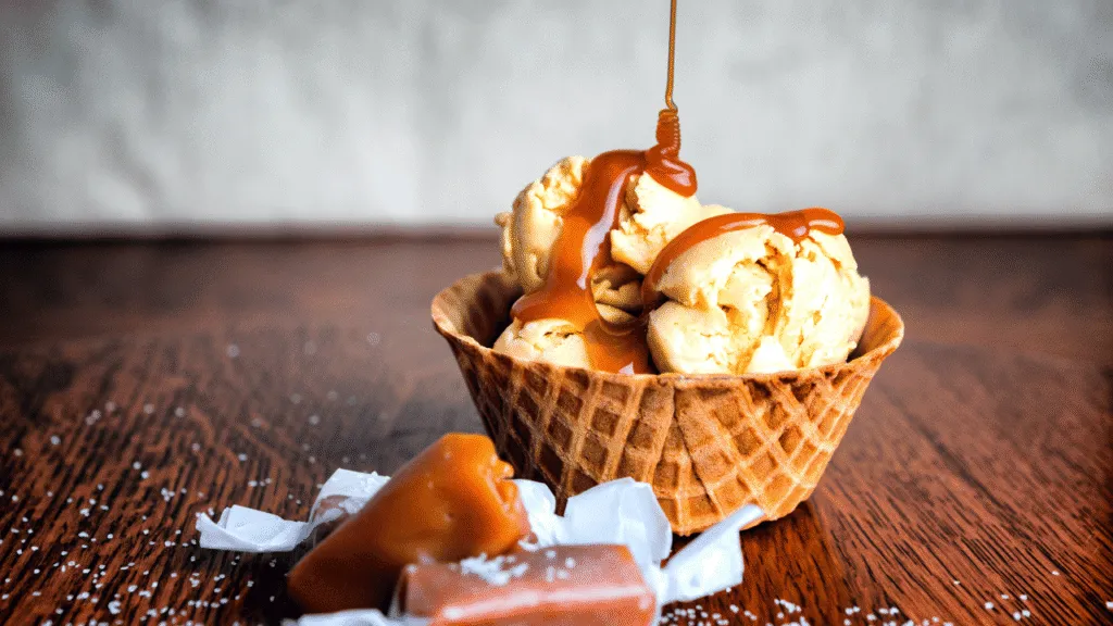 A churned tub of creamy, pale ice cream, flecked with tiny vanilla bean specks. The surface is slightly textured, with a soft, pillowy appearance, as if just freshly scooped from the machine. Soft, diffused lighting casts a warm, golden glow, highlighting the luscious, silky texture. The ice cream is set against a backdrop of a stainless steel ice cream maker, its chrome finish gleaming. The entire scene has a simple, clean, and inviting aesthetic, perfectly capturing the step-by-step journey from custard base to churned perfection. Step-by-Step Baileys and Ice Cream Recipe: From Custard Base to Churned Perfection