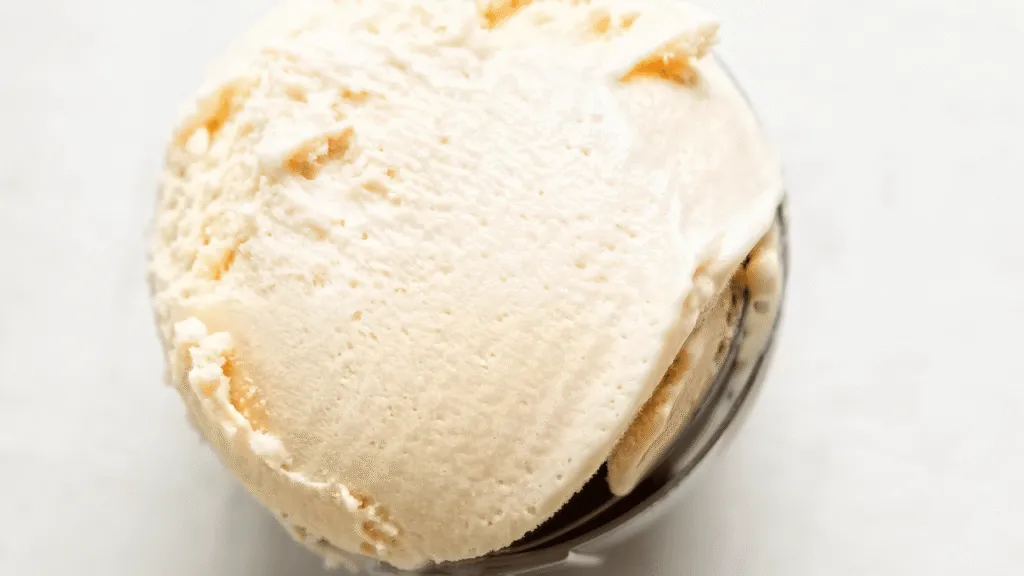 A bottle of pure vanilla extract on a wooden table, illuminated by soft, natural lighting. The glass container has a classic teardrop shape, with a deep amber liquid visible through the transparent glass. The label features a simple, elegant design in black and white, showcasing the high-quality nature of the product. The background is a slightly blurred, warm-toned wooden surface, adding a cozy, rustic feel to the composition. The overall scene exudes a sense of simplicity and quality, reflecting the essential nature of the key ingredient in a homemade, creamy ice cream made with condensed milk. Homemade Ice Cream Condensed Milk recipe Simple ingredients for ultra‑creamy results