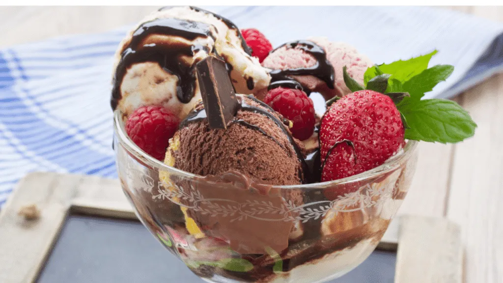 A close-up and highly detailed depiction of a ripe vanilla bean pod, split open to reveal its tiny black seeds, resting on a textured wooden surface. The background features a softly blurred arrangement of dairy-free ice cream scoops, showcasing creamy, rich textures in shades of ivory and beige. Natural light illuminates the scene, casting gentle shadows that highlight the glossy surface of the vanilla bean and enhance the inviting appearance of the ice cream. The mood conveys warmth and indulgence, capturing the essence of enjoying a delicious yet non-dairy dessert. Use a shallow depth of field to bring attention to the vanilla bean and the ice cream, creating a cozy and enticing atmosphere. Brands and pints we’d skip (and why texture matters as much as flavor)